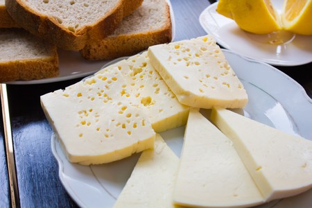 various pieces of cheese lying on a plate next to the lemon and slices of brown bread on a white plate and a stylish black table.の写真素材