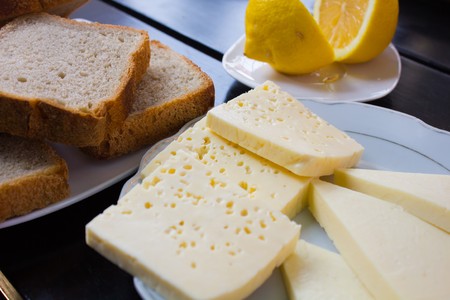 various pieces of cheese lying on a plate next to the lemon and slices of brown bread on a white plate and a stylish black table.の写真素材