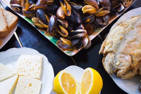 various pieces of cheese lying on a plate next to the lemon and slices of brown bread with mussels and grilled fishの写真素材