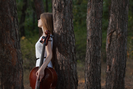 Woman cellist in white dress with cello outdoorsの写真素材