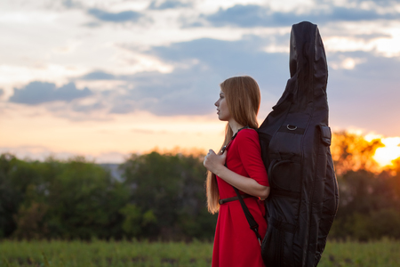 Woman in red dress travelling with cello outdoorsの写真素材