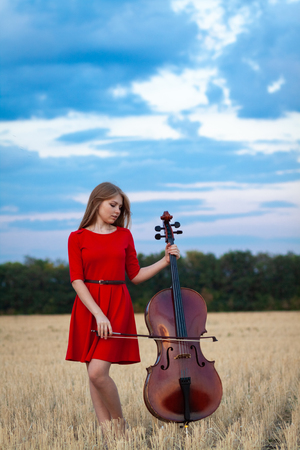 Professional female cello player in red dress with instrument outdoorsの写真素材