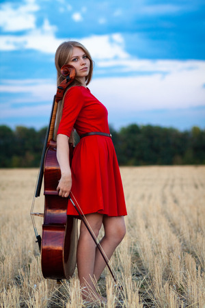 Professional female cello player in red dress with instrument outdoorsの写真素材