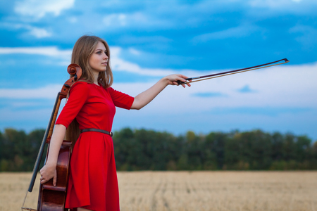 Beautiful woman professional musician in red dress with cello outdoorsの写真素材