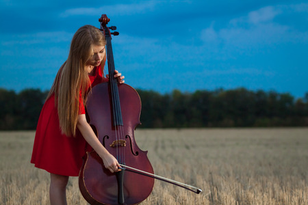 Professional female cello player in red dress with instrument outdoorsの写真素材