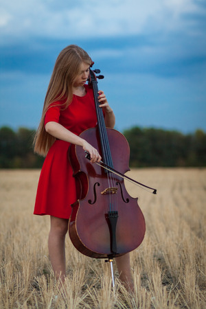 Professional female cello player in red dress with instrument outdoorsの写真素材