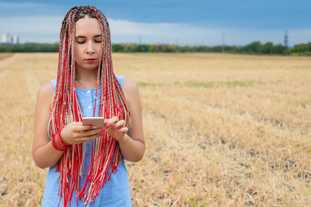 Caucasian woman with african pigtails using smartphone outdoorsの写真素材