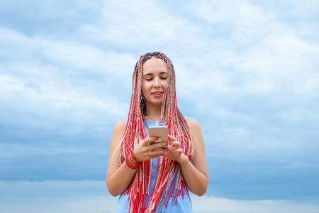 Caucasian woman with african pigtails using smartphone outdoorsの写真素材