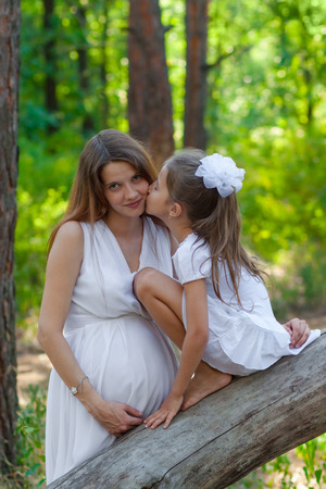 Little daughter kissing her pregnant mother outdoorsの写真素材