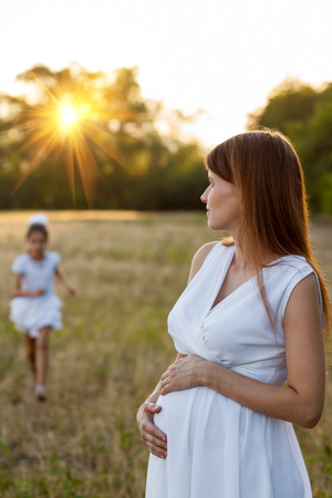 Pregnant woman and her daughter watching the sunset outdoorsの写真素材