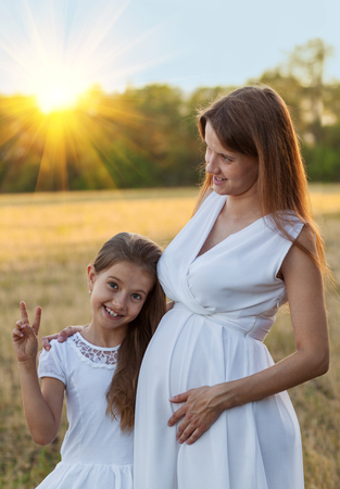 Happy little girl with her pregnant mother showing victory signの写真素材