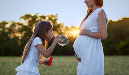 Pregnant woman and her daughter blowing bubbles at sunsetの写真素材