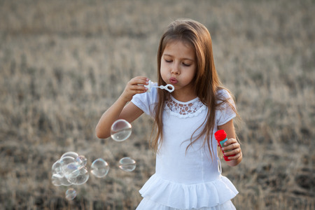 Girl in white dress blowing bubbles at sunsetの写真素材