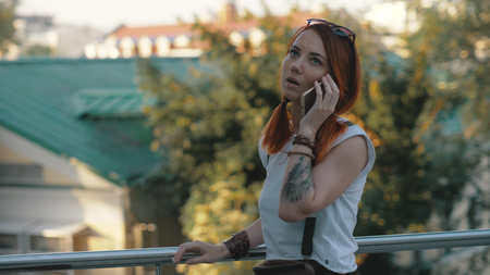 Young redhaired woman riding bicycle in city. Woman with mobile phoneの写真素材