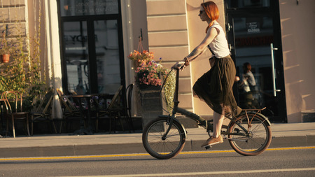 Woman cyclist walking beside riding bike on city road. Woman bike cityの写真素材