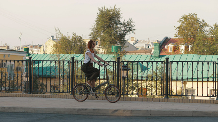 Redhaired woman riding a bike in city on background buildings and roof houseの写真素材