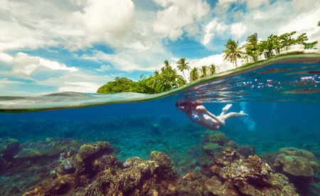 Split underwater photo of a girl snorkeling with mask in tropical ocean enjoying summer vacation on exotic islandの写真素材