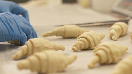 Baker putting croissant on paper in tray for baking in oven on bakery kitchen