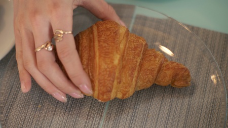 Female hand taking croissant from glass plate at table in cafe close upの写真素材