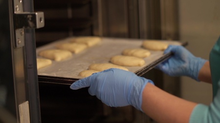 Baker oppening oven and taking tray with baked patties on restaurant kitchen