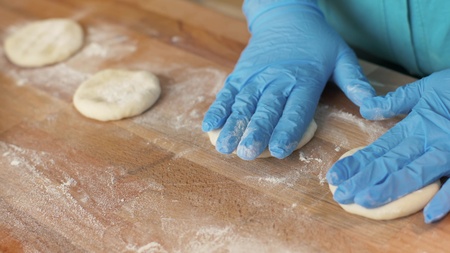 Baker hand in gloves rolling dough for pastries on wooden table in bakery shop