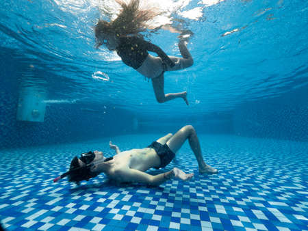 Underwater view of young man and woman in the transparent blue swimming pool.の写真素材