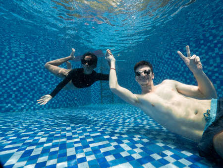 Young couple wearing sungaless underwater in swimming pool holding hands and smiling.の写真素材