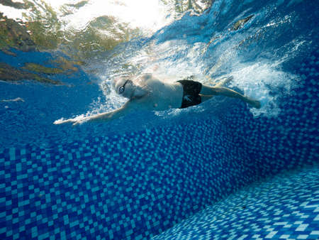 A Caucasian man in short and goggle swimming in the blue swimming pool outdoorの写真素材
