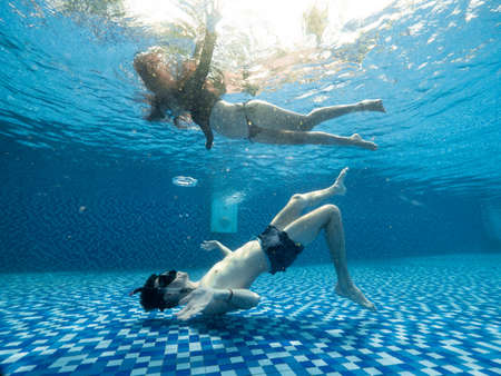 Young man and woman underwater view in the pristine blue swimming pool.の写真素材