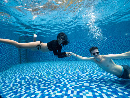 Smiling young man and woman in swimwear and sunglasses holding hands underwater.の写真素材