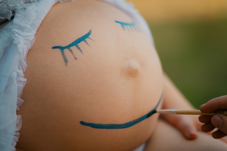 Pregnant woman belly closeup with smiling funny face drawingの写真素材