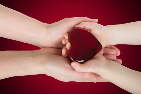 Mother's hands holding baby hands with glass heart shape in itの写真素材