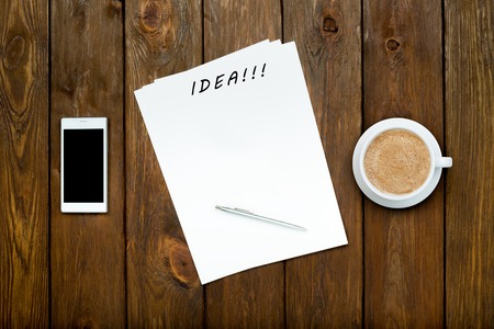 Smartphone, latte coffee and blank paper sheets with a pen on woodの写真素材