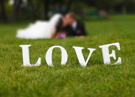 Wedding couple unfocused and big white "love" word on the grassの写真素材