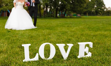 Wedding couple unfocused and big white "love" word on the grassの写真素材