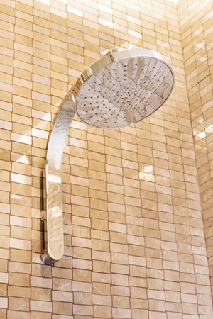 Modern shower head mounted on a beige tile wall in a bathroomの写真素材
