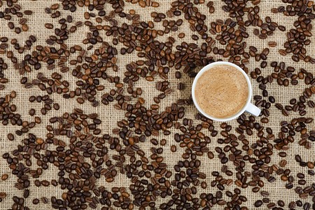 Coffee cup and beans scattered on sacking backgroundの写真素材