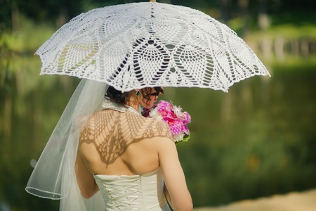Beautiful bride with white lacy umbrella  from the backの写真素材