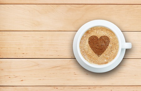 Coffee concept - cup of latte with heart symbol on froth at wooden tableの写真素材