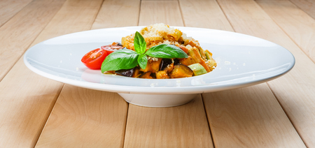 Traditional italian pasta with aubergine, zucchini, cherry tomatoes and parmesan decorated with basil.の写真素材
