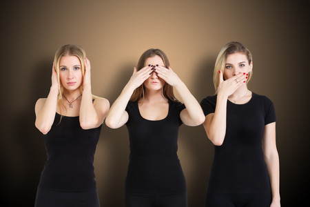 Three young woman in black clothes isolated at brown background showing blind, deaf and dumb: wise monkey scene - hear no evil, see no evil, speak no evilの写真素材