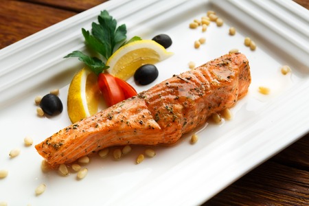 Restaurant food, salmon dish. Hot fish dish. Barbecue grilled fish dish. Restaurant food catering. Salmon barbecue grill roasted with lemon and olives. Grilled salmon served in restaurant closeup.の写真素材