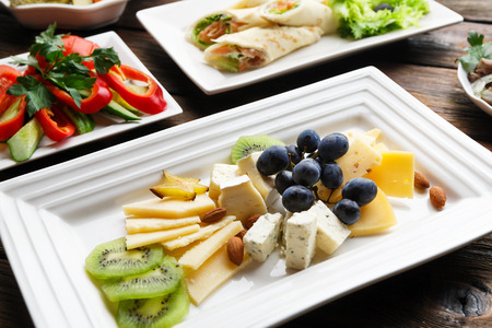 Restaurant food - cheese plate with kiwi, grapes and almond at wooden table. Vegetarian, healthy...
