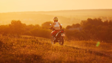 Woman biker rides in fields. Sporty woman biker at motobike. Countryside, country road.  sunset, female motorcycle rider, motorbike rider travel the world, girl resting, freedom lifestyle, back viewの写真素材