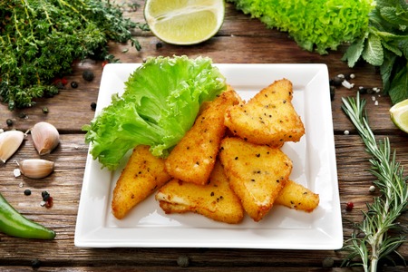Fried cheese sticks at square plate. Dish served at rustic wooden background with fresh green vegetables and herbs at background.の写真素材