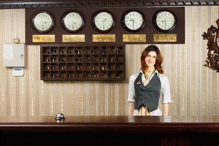 Hotel reception. Female receptionist at reception. Modern hotel reception counter desk with bell. Woman receptionist, concierge at desk. Travel, hospitality, hotel booking concept.の写真素材