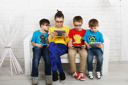 Group of kids in eye glasses look into their phones and tablets.の写真素材