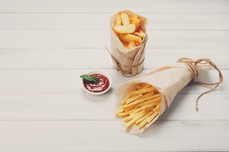 Potato wedges and french fries wrapped in brown wrapping paper on white shabby chic wood.の写真素材