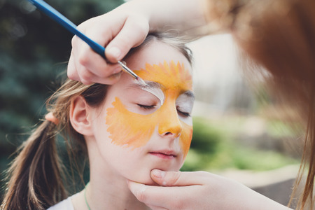 artist's hand draws face painting to little girl.