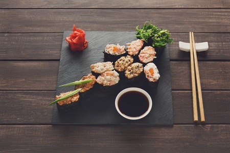Japanese food restaurant, sushi gunkan roll plate, platter set. Creative food. Set with chopsticks, ginger, soy, wasabi. Sushi at rustic wood background and black stone. POV, horizontal imageの写真素材